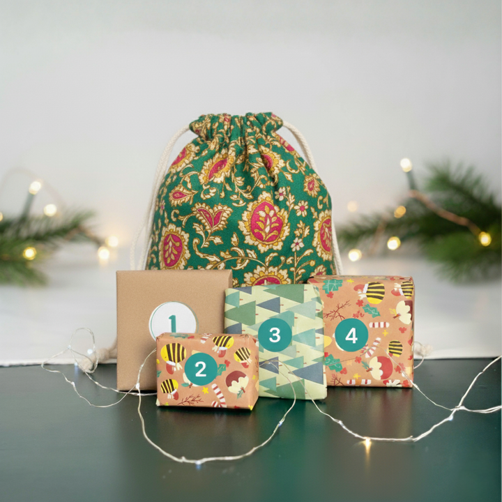 Decorative boxes with numbers and a patterned drawstring bag on a surface with string lights and greenery.