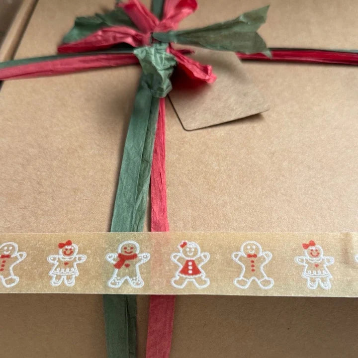 Gift box wrapped in brown paper with a gingerbread man festive paper tape, green and red ribbon and tag.