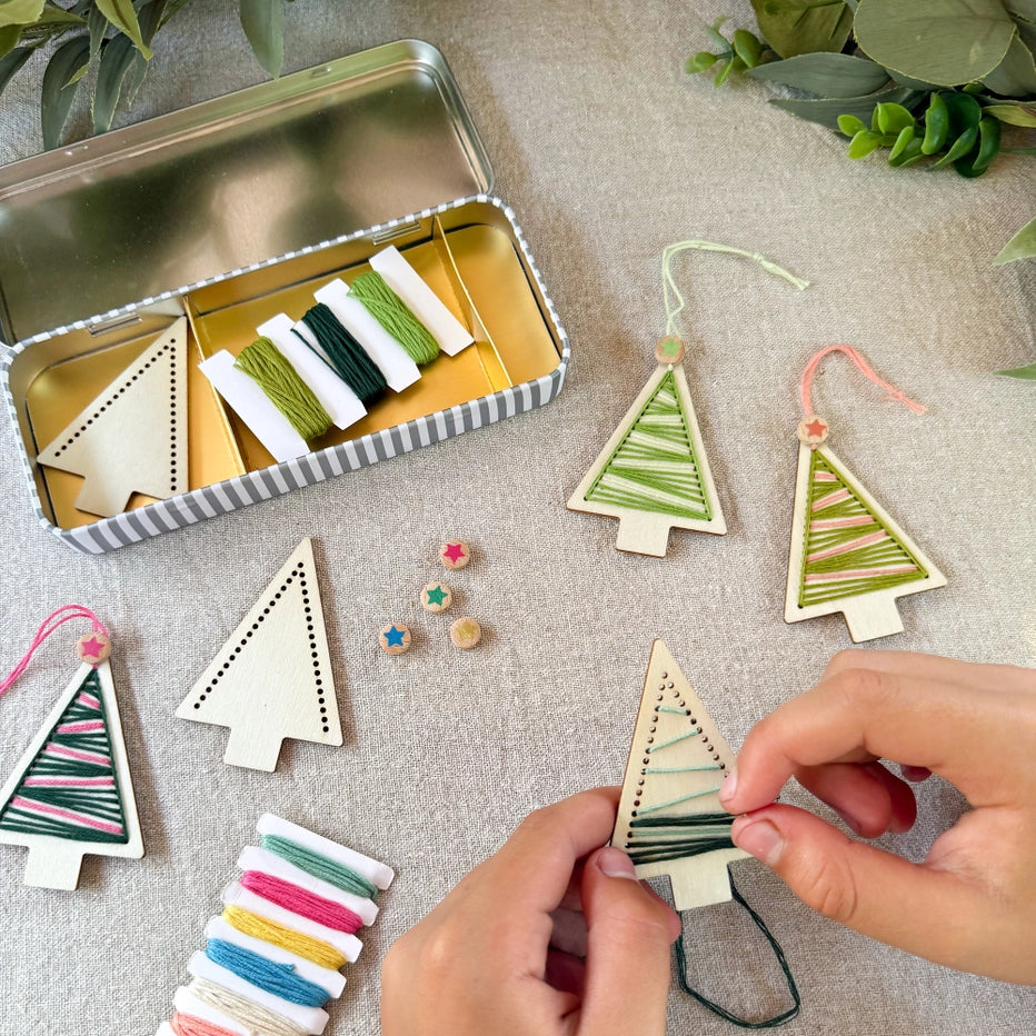 Handmade Christmas tree decorations with embroidery threads on a textured surface.
