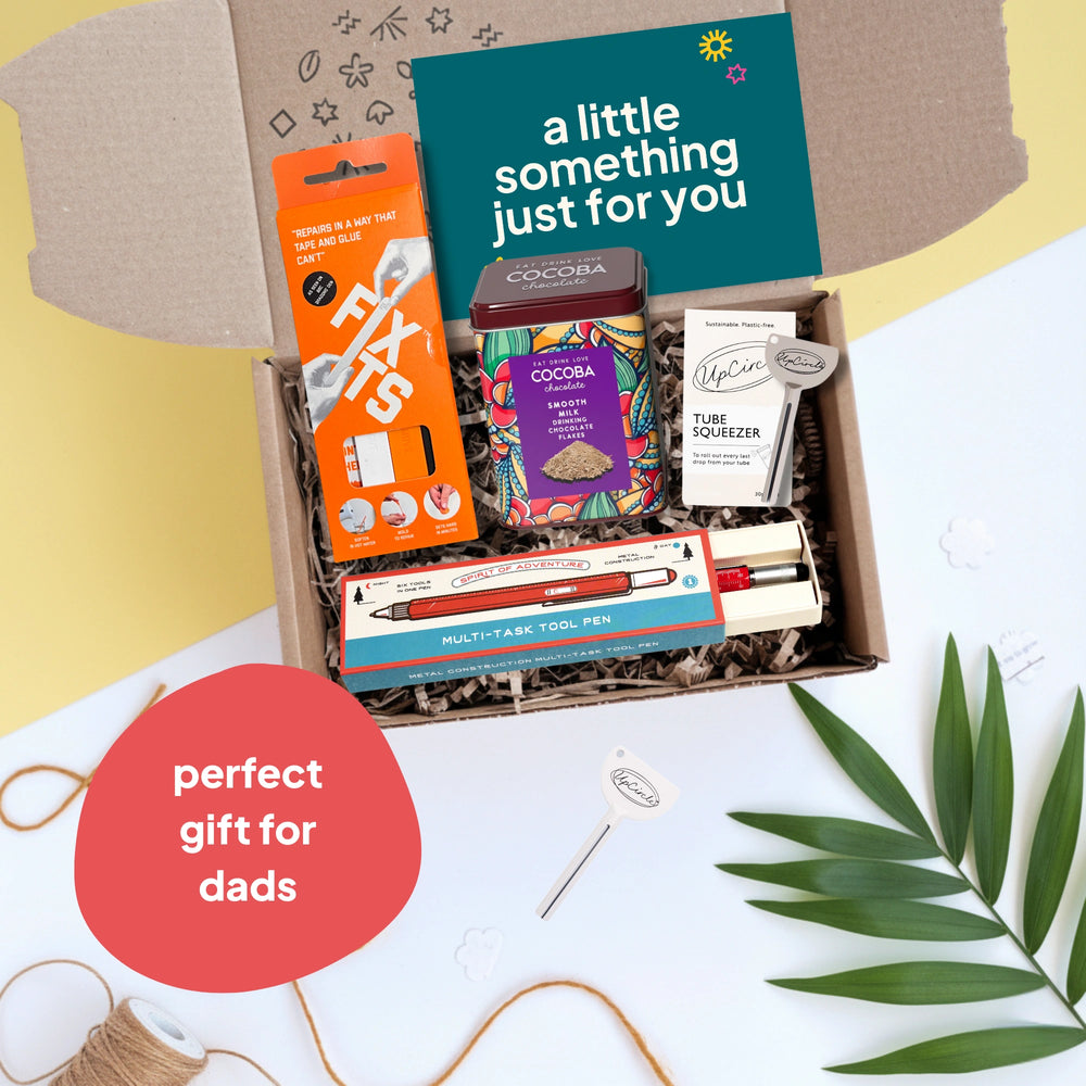 dad's gadgets gift box with fix its, tin of hot chocolate, tube squeezer and a multi tool pen on a light background. Perfect gift for dads