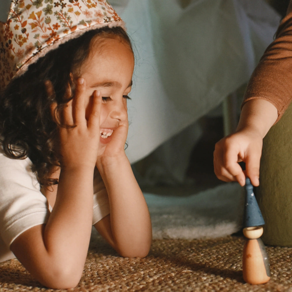 Child playing with a wooden peg doll toy on a carpeted floor