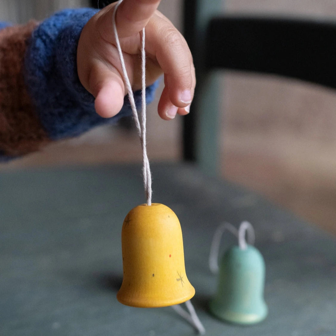 childs hand holding a yellow Jingle Joy Bell wooden bell shaped christmas decorations made by grapat toys. Suitable for kids aged 3 and over 