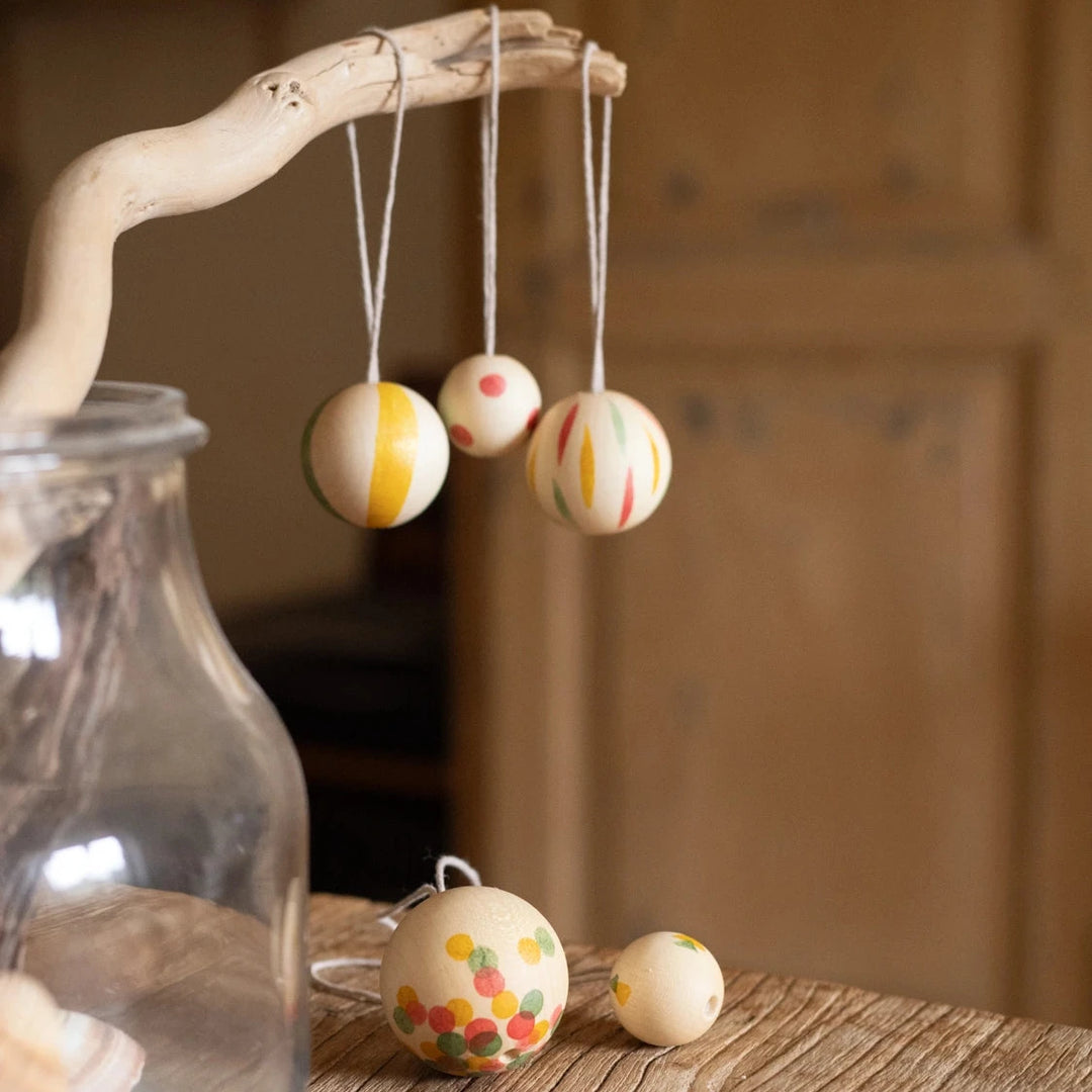 Set of 5 'wonder balls' wooden christmas decorations hand painted with colourful stripes and spots.  The decorations are hanging on a reclaimed tree branch indoors. 