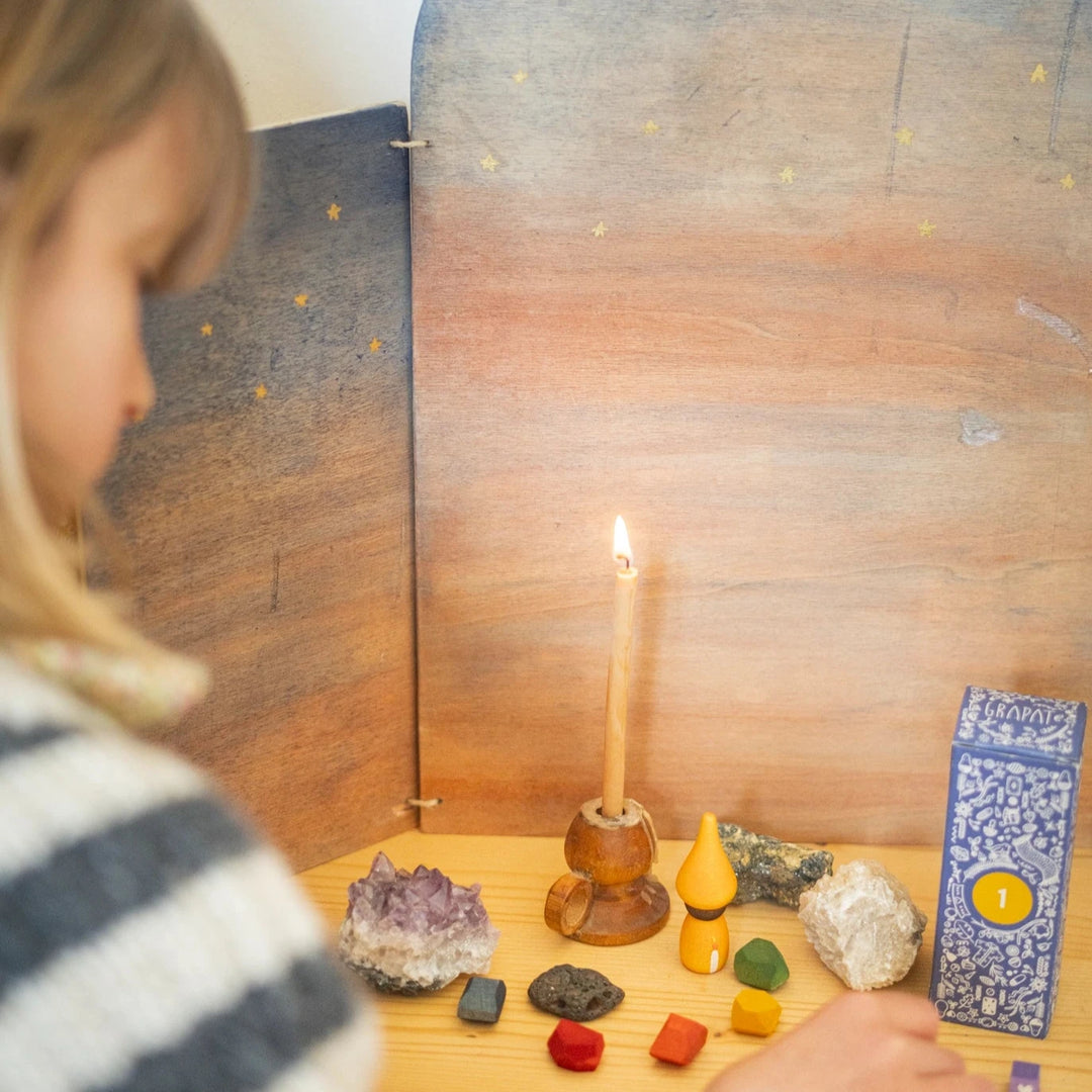 woman arranging wooden peg dolls and elements from the Grapat Advent calendar  on a festive themed table with a lit candle