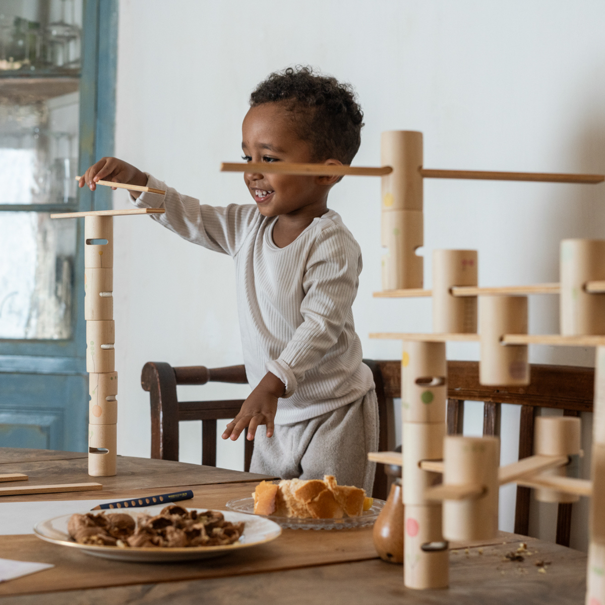 child with brown skin and shirt black hair playing with grapat woodland - a wooden building set including tubes and platforms for building play