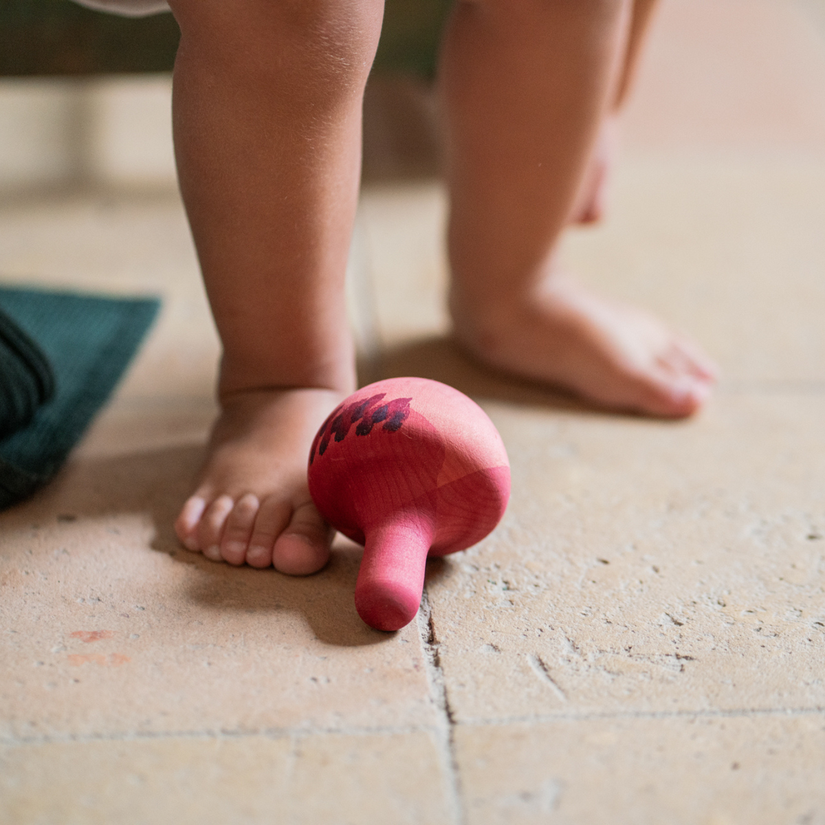 toddlers foot next to pink wooden spinning top toy made by grapat. 
