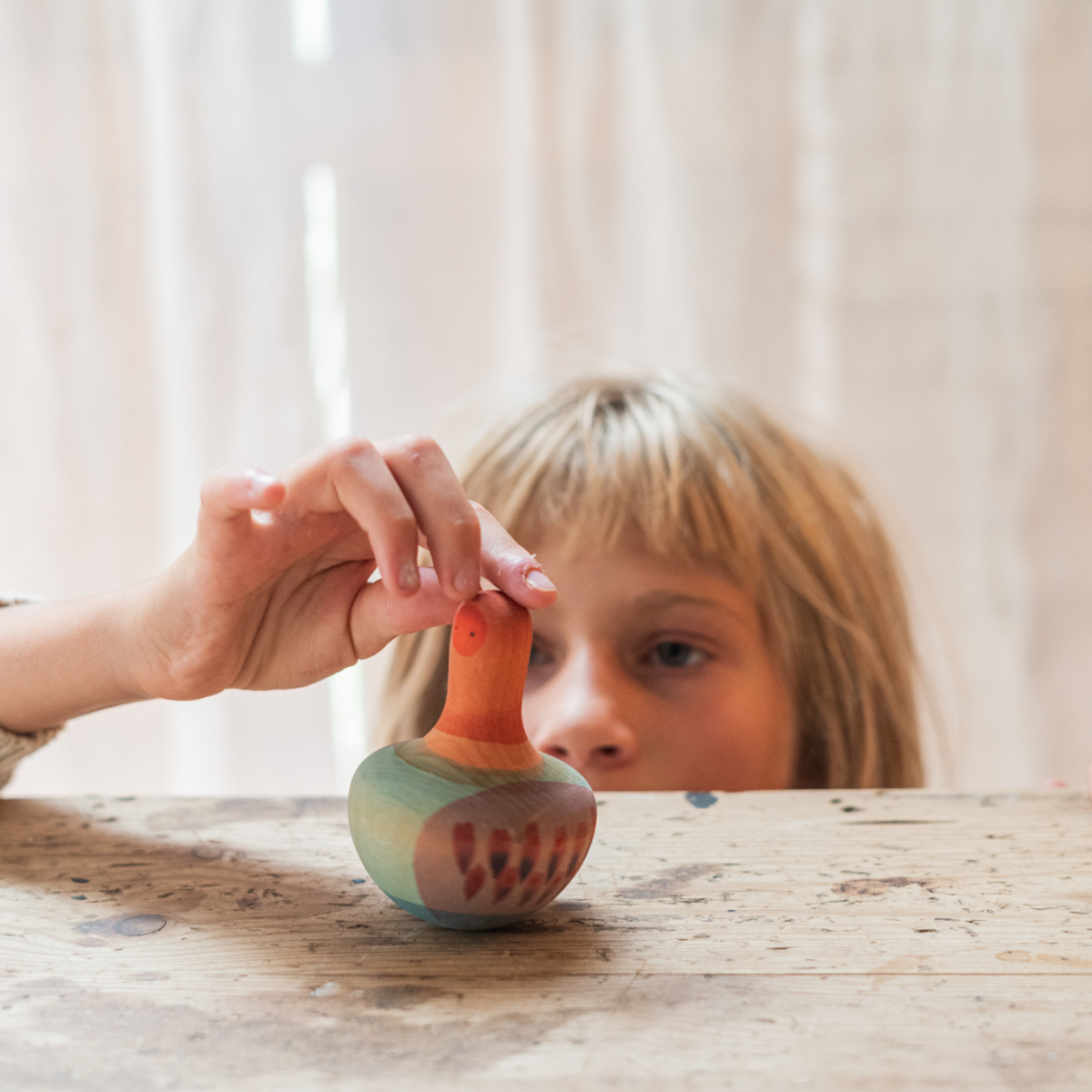 girl playing with orange, pink and blue hand painted bird-themed wooden spinning top toy 