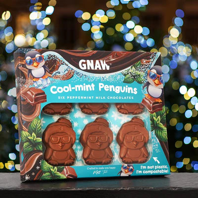 Packaged chocolate penguins with 'GNAW' branding against a blurred festive background