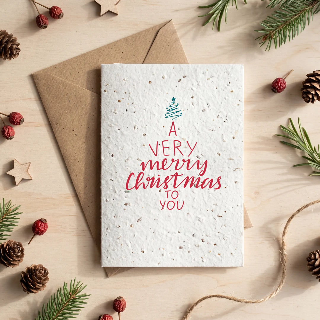 A textured white Christmas greeting card with a blue tree and red lettering reading &