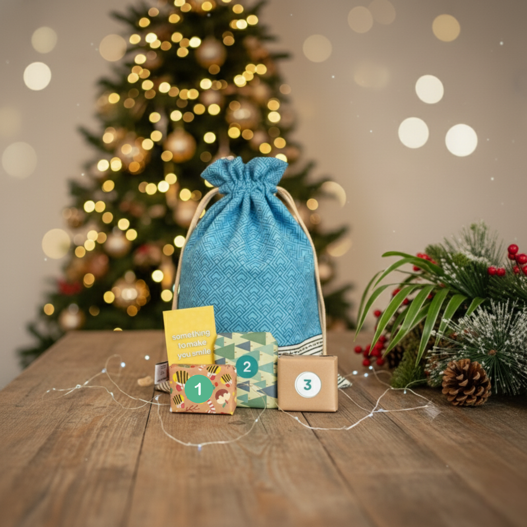 Blue drawstring bag with numbered boxes from the Smallkind 12 days of self care advent calendar on a wooden table in front of a Christmas tree.