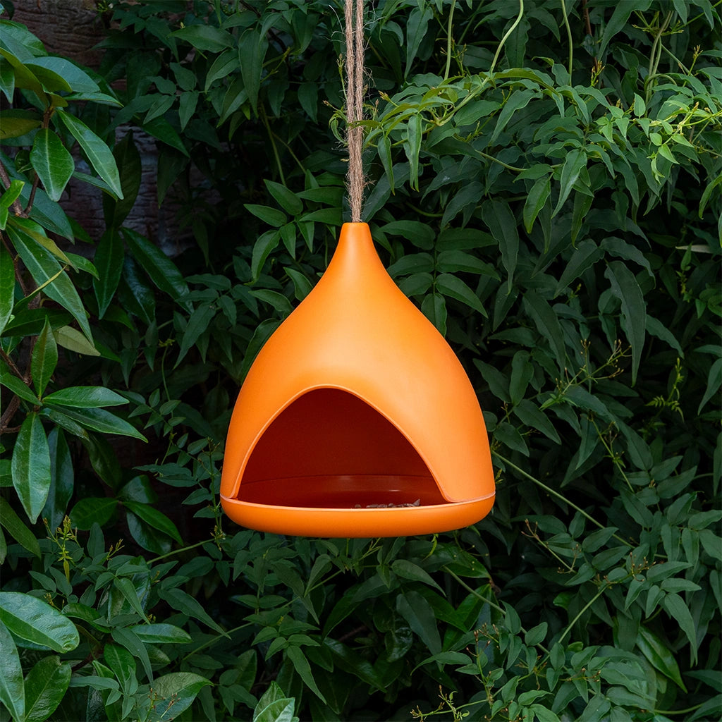 modern orange bamboo bird feeder  hanging from an outdoor tree. eco friendly garden decor. 