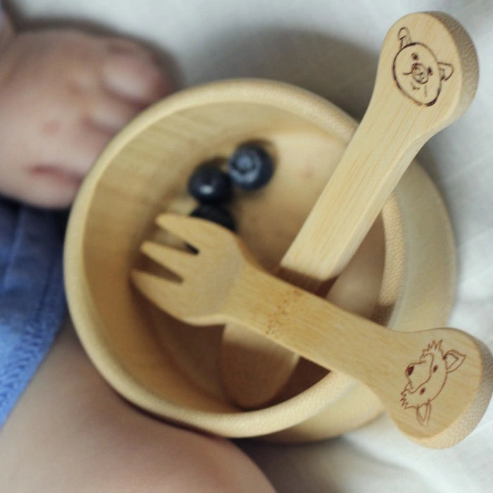 Kids Bamboo Fork + Spoon Set with animal faces etched into the handles. The cutlery is in a bamboo bowl 