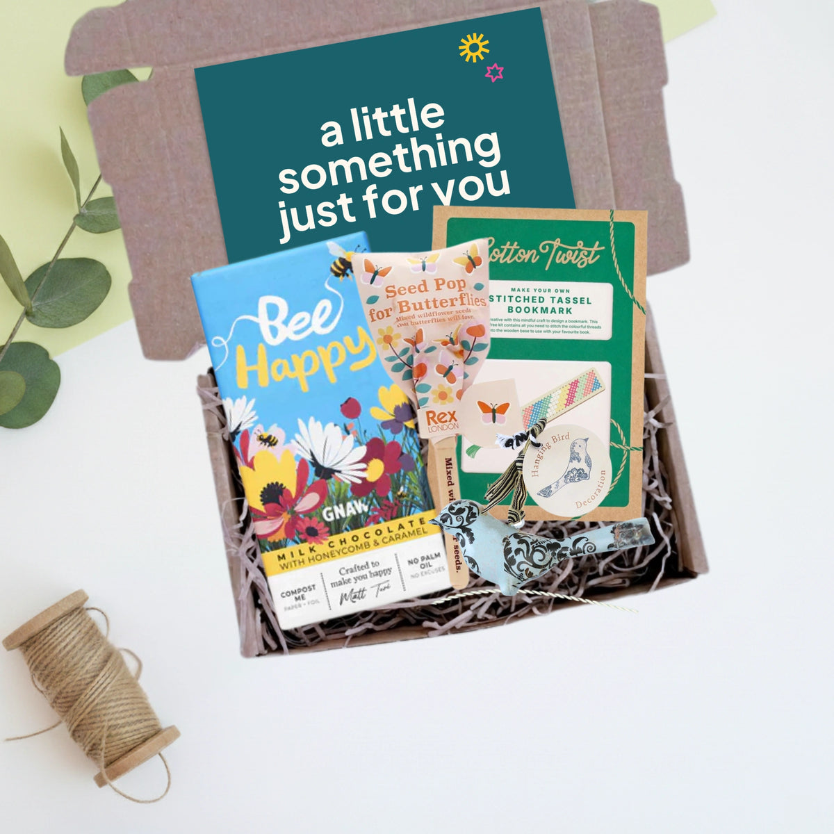 Gift box with a bookmark craft kit, chocolate, seed bomb and a bird decoration on a light background