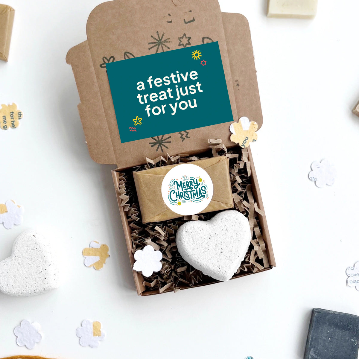Merry Christmas hug in a box with a heart-shaped bath bomb and a small soap bar on a white background with decorative elements.