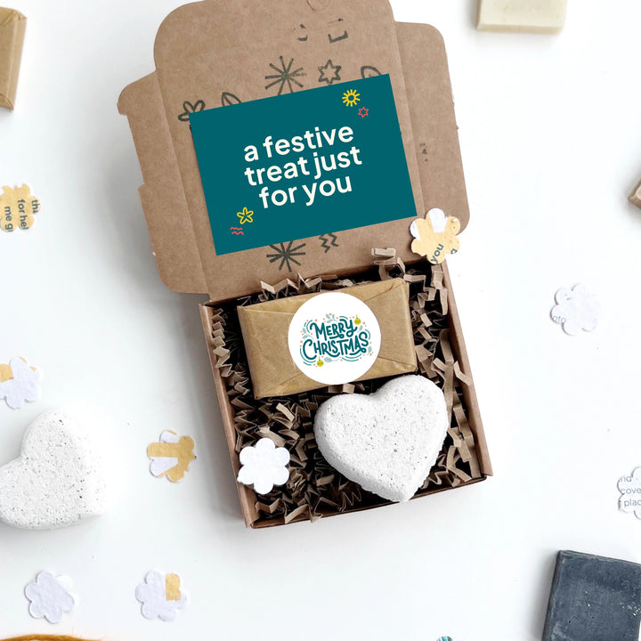 Merry Christmas hug in a box with a heart-shaped bath bomb and a small soap bar on a white background with decorative elements.