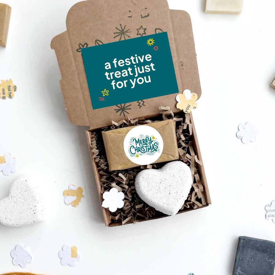 Merry Christmas hug in a box with a heart-shaped bath bomb and a small soap bar on a white background with decorative elements.