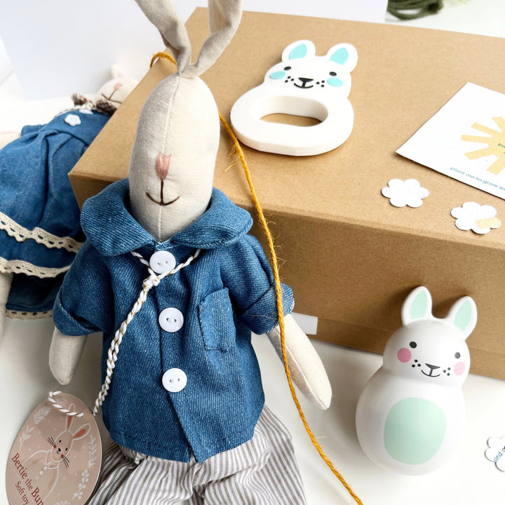 Stuffed rabbit toy in a blue coat with a gift box and other bunny toys in the background.