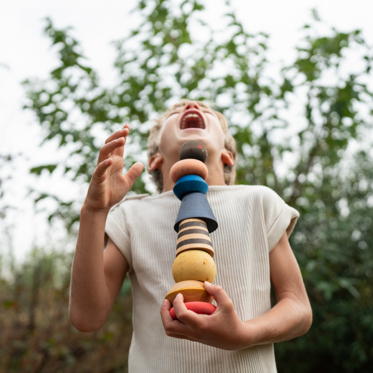 boy with white skin and blond hair holding a tower of colourful painted wooden blocks from the grapat serendipity playset 