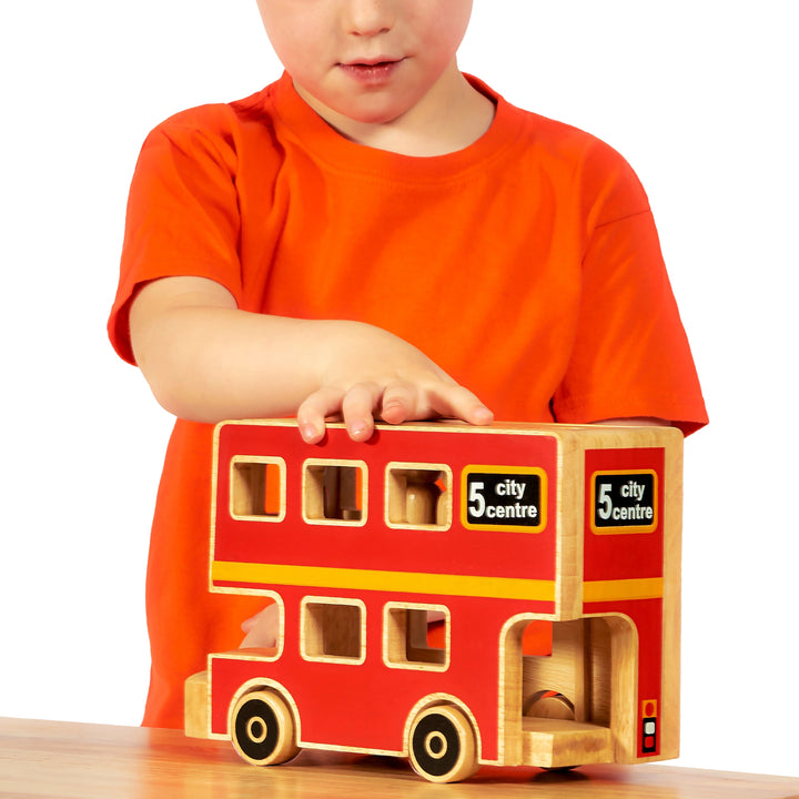 boy playing with a red London bus toy with wooden people inside