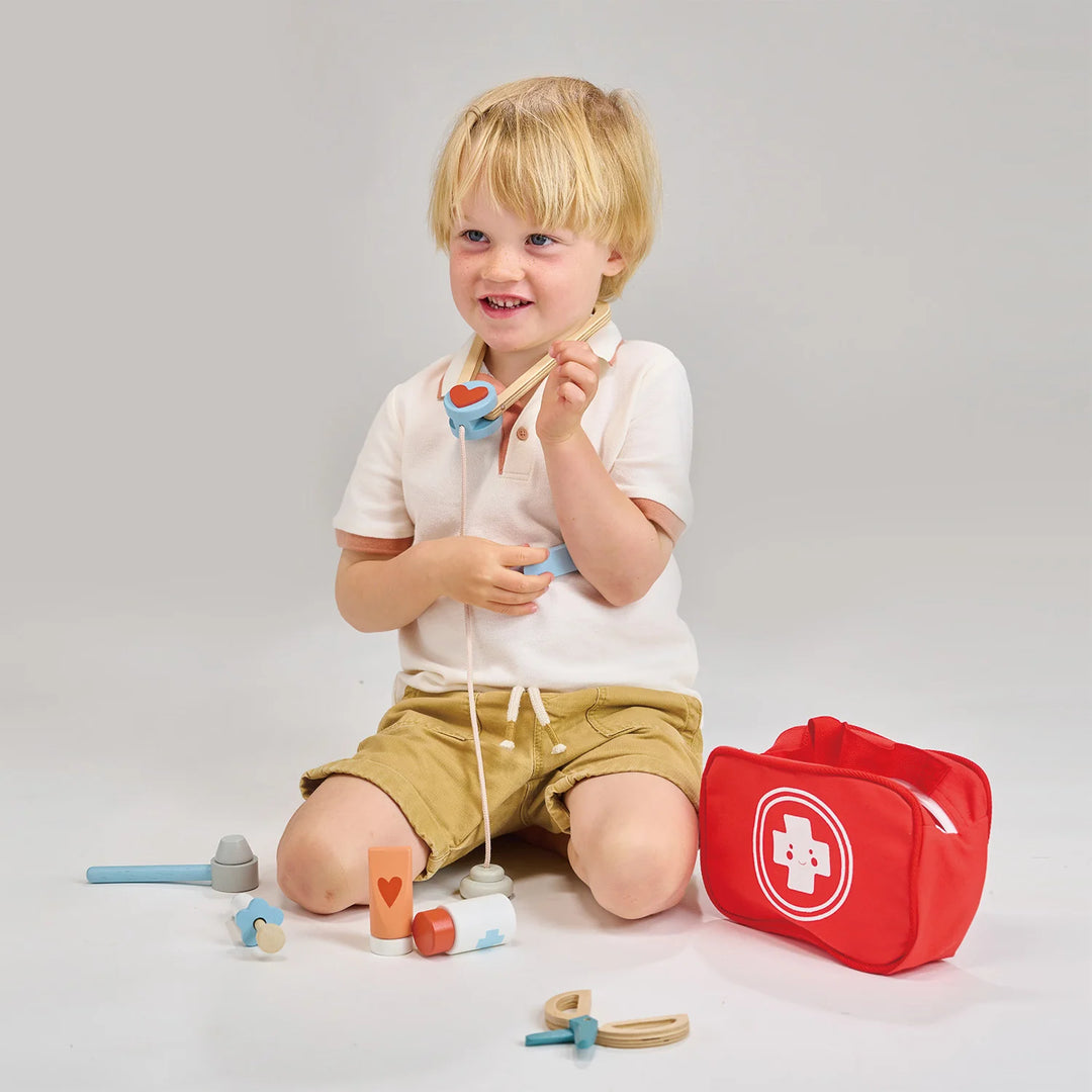 Child playing with toy medical kit and tools on a plain background
