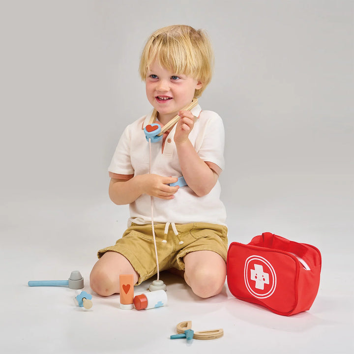 Child playing with toy medical kit and tools on a plain background