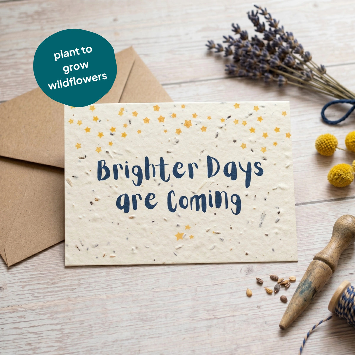 Seed paper card with 'Brighter Days are Coming' text, surrounded by dried lavender and a brown envelope on a wooden surface.