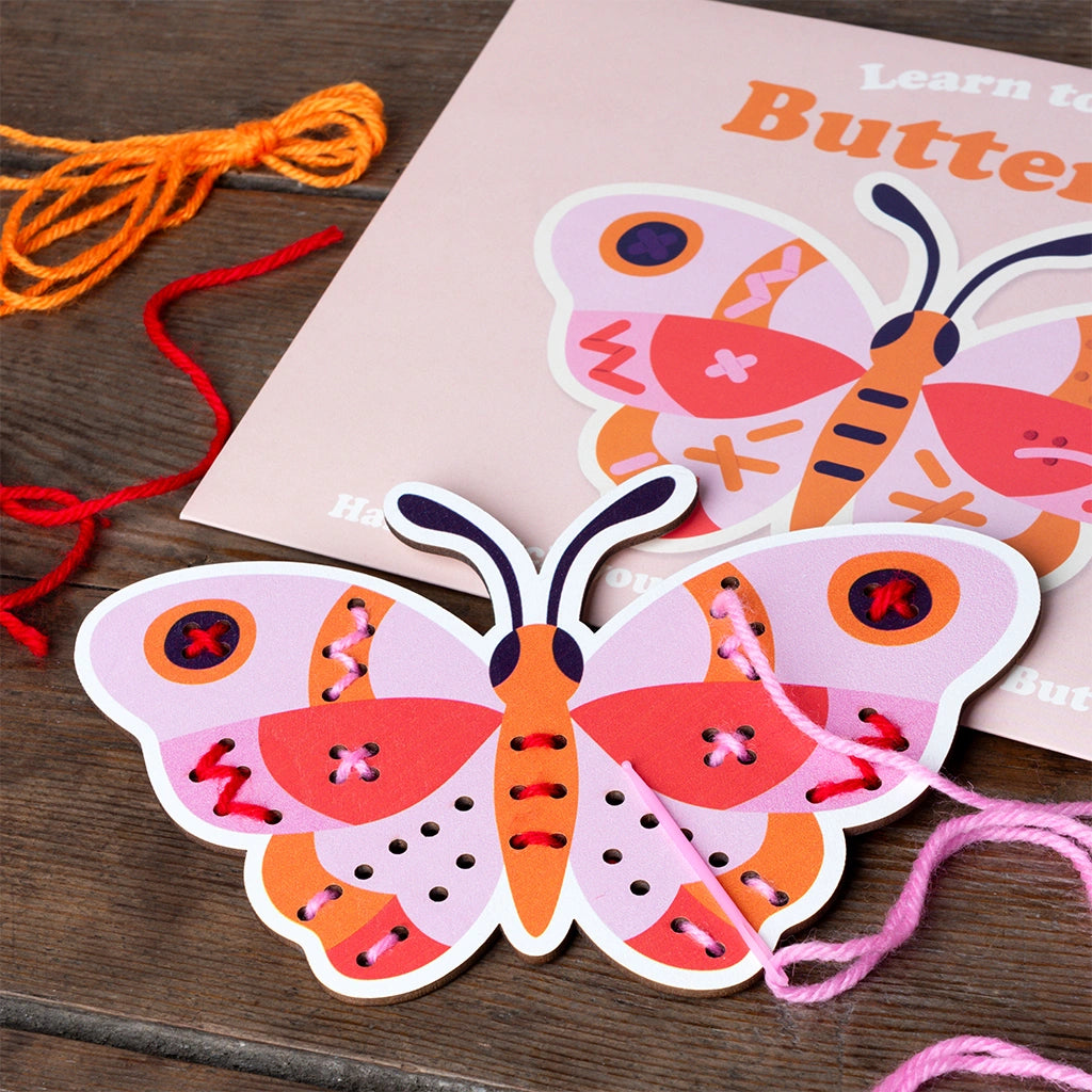 Wooden Learn to Sew Kit on a wooden table - wooden butterfly board, needle, pink yarn, and gift packaging