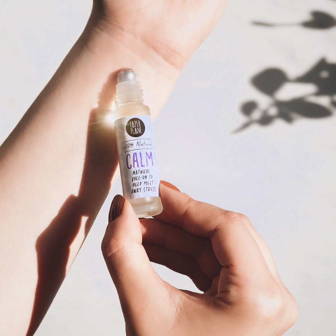 A hand holds a small clear bottle of essential oil labeled &