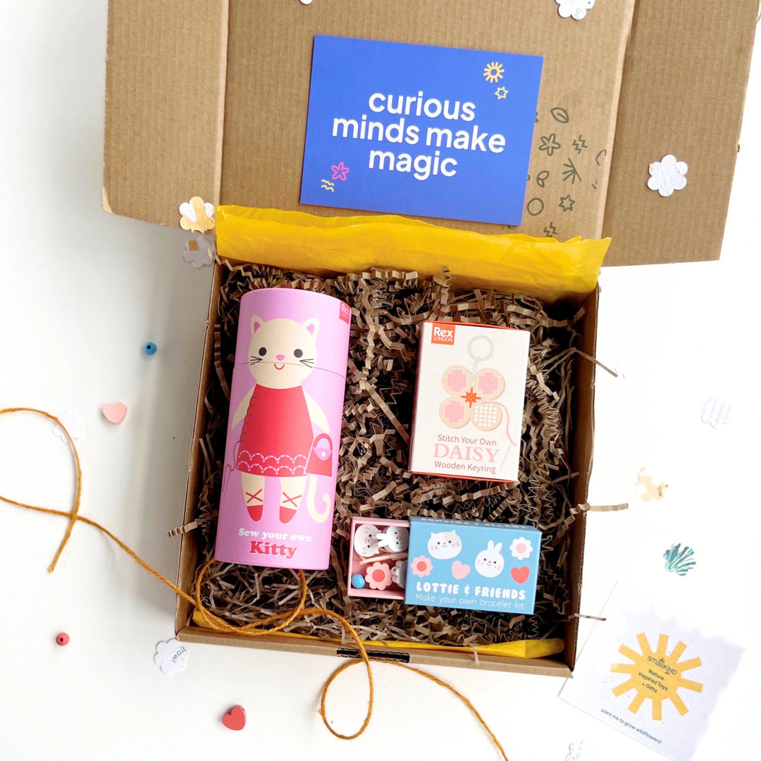 Open gift box with a sew your own cat kit, daisy keyring kit and cute bunny jewellery making set on a white background.