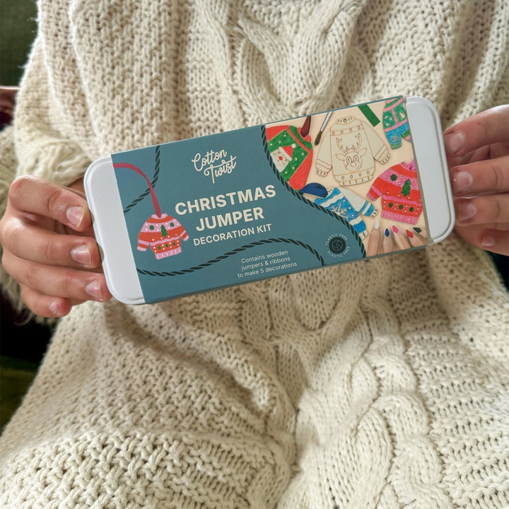 child's hands holding a Cotton Twist Christmas Jumper Decoration craft kit in a tin.