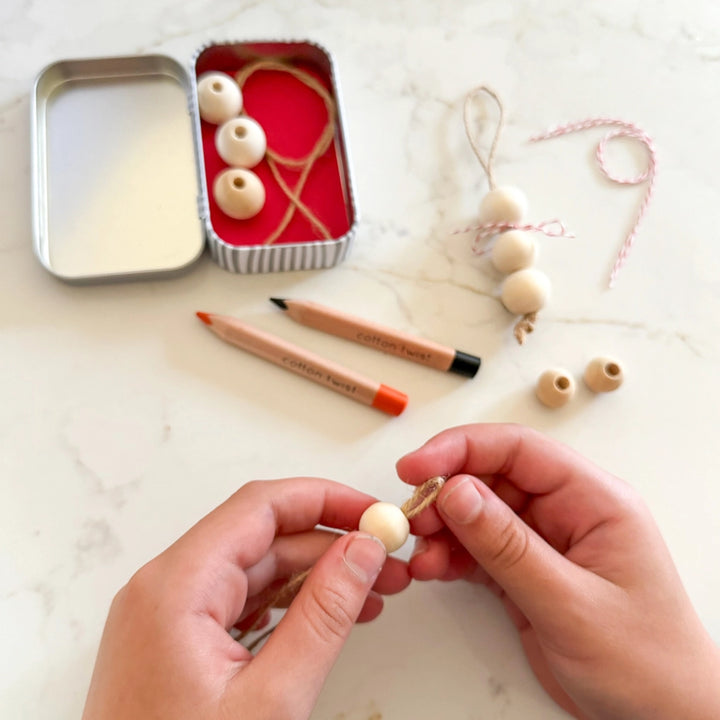 child's hands making wooden beaded decorations with supplies on a white surface