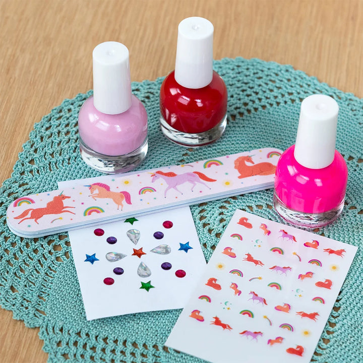 A nail art kit featuring two nail polish bottles (one light pink, one bright pink), a unicorn-themed nail file, and two sheets of colorful star and unicorn stickers on a teal crocheted doily over a wooden surface.