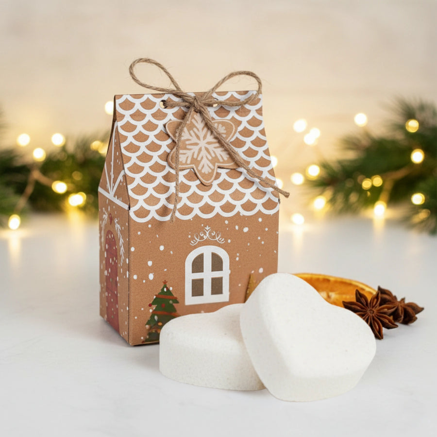 Gingerbread house-shaped gift box with heart shaped Christmas bath bomb on a festive background