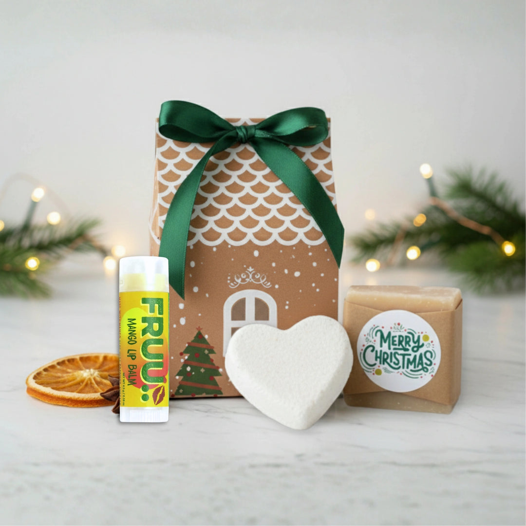 Christmas-themed gift set with a house-shaped box, heart-shaped bath bomb, merry Christmas soap and lip balm on a white surface.