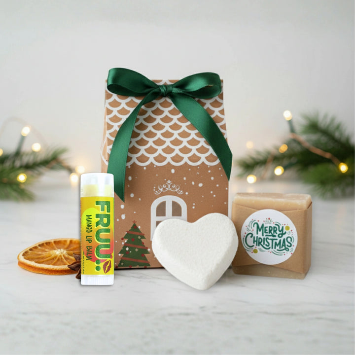 Christmas-themed gift set with a house-shaped box, heart-shaped bath bomb, merry Christmas soap and lip balm on a white surface.