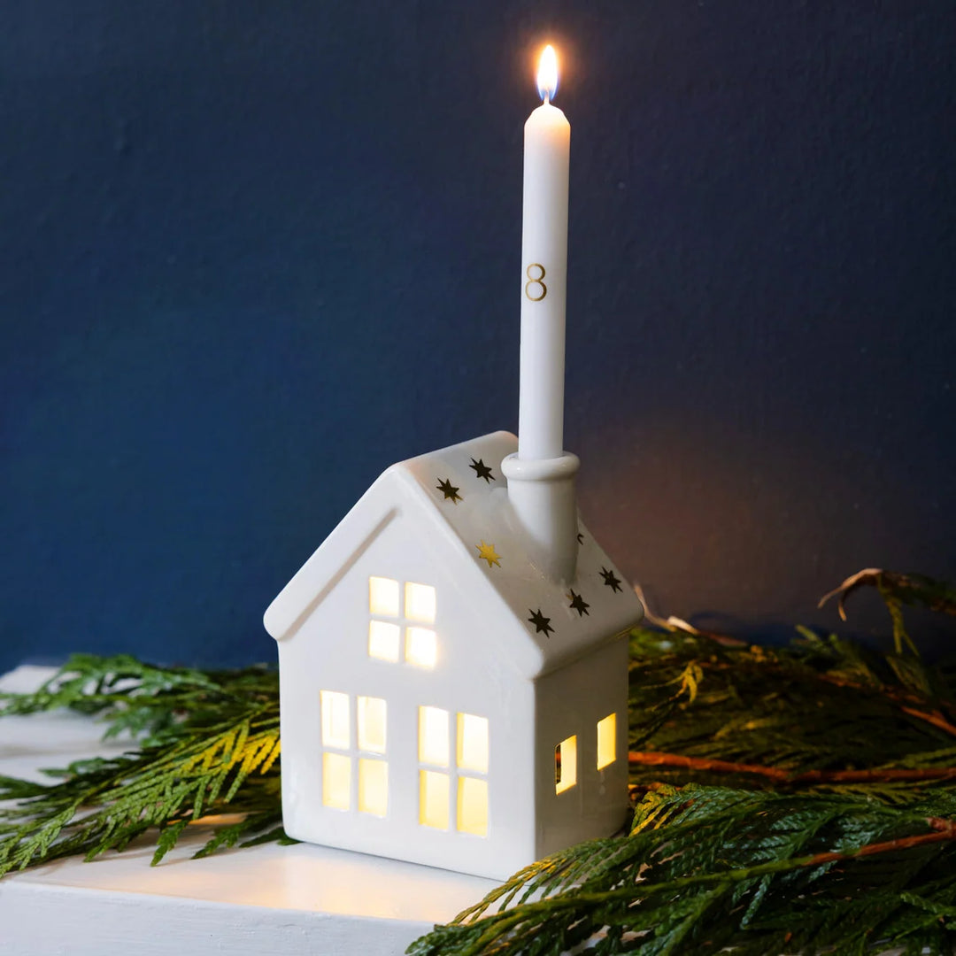 White house-shaped lantern with a lit candle on top, surrounded by greenery against a dark sky.