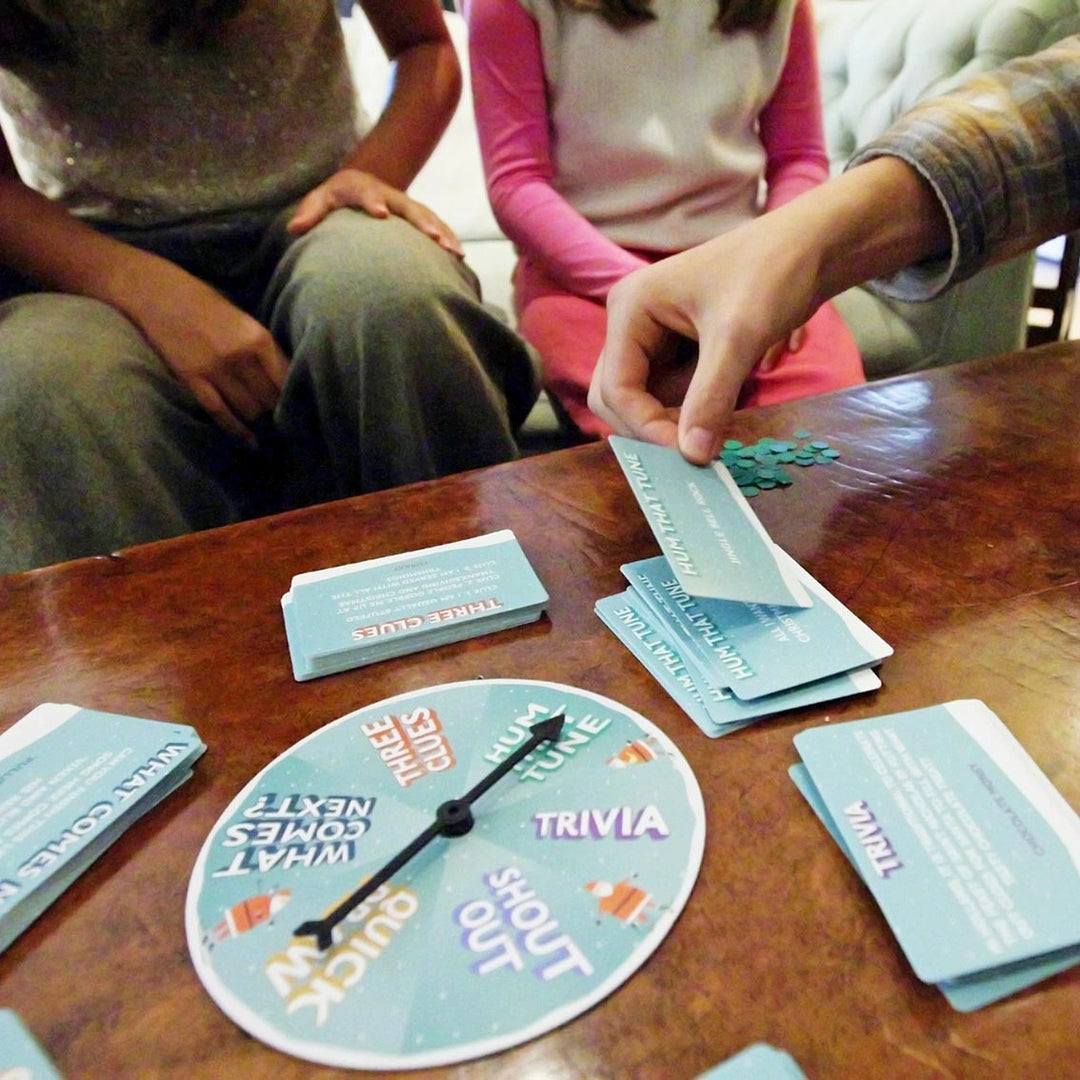 People playing a trivia game with cards and a spinner on a wooden table.