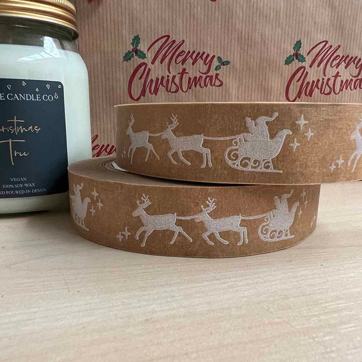 Two rolls of brown paper with Christmas Santa and sleigh designs next to a candle.
