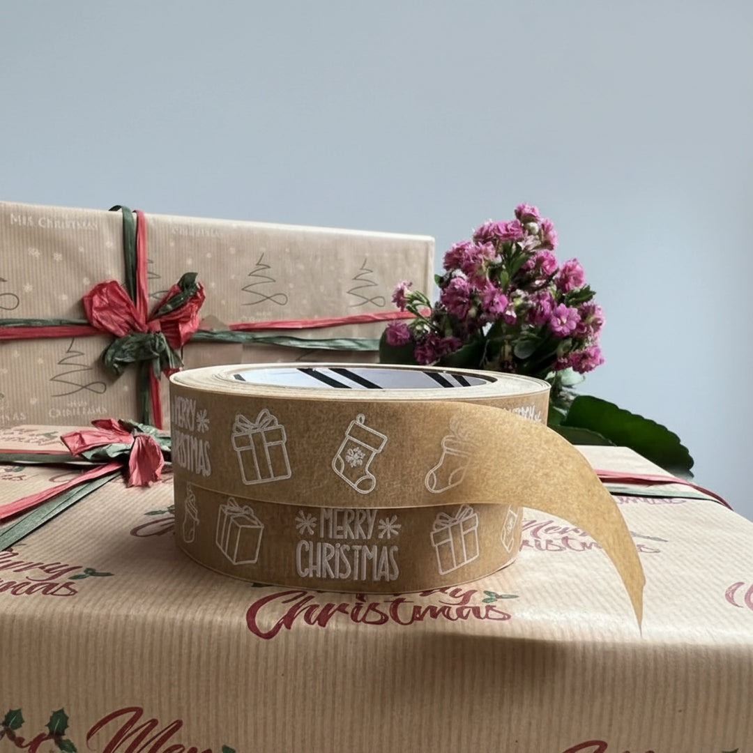 Roll of Christmas-themed tape with wrapped gifts and flowers in the background