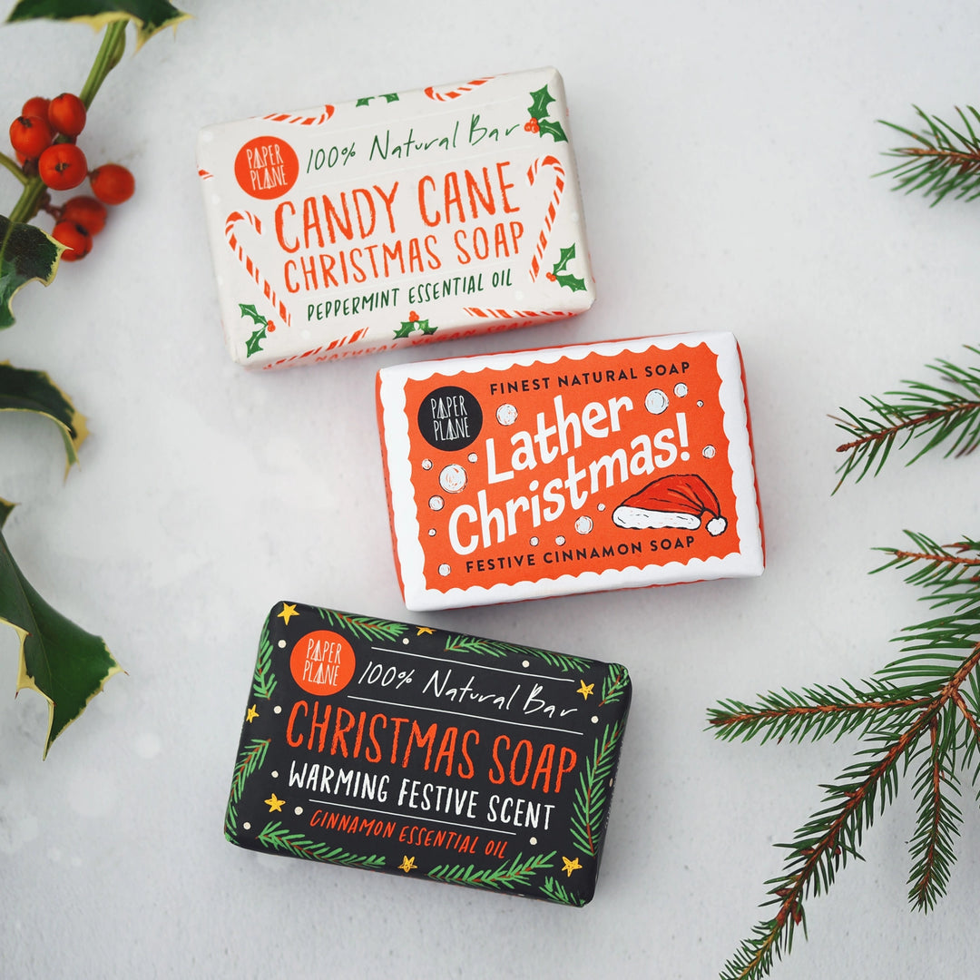 Three Christmas-themed soap bars with decorative packaging on a white background with festive elements.