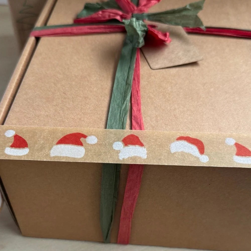 Gift box wrapped in brown paper with a Santa hat festive paper tape, green and red ribbon and tag.
