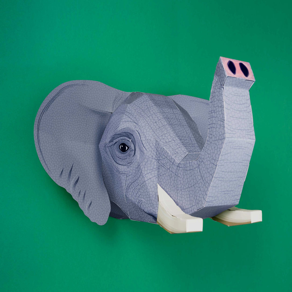 Side View of the Create Your Own Extraordinary Elephant Craft Kit by Clockwork Soldier. The finished elephant head hangs on a green wall.