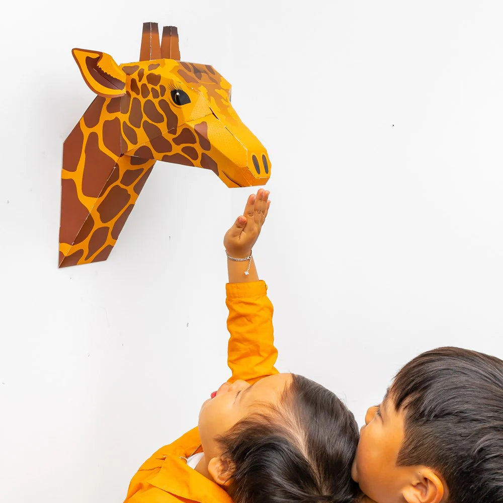 children reaching to touch a Create Your Own Gentle Giraffe Craft Kit hung on a white wall
