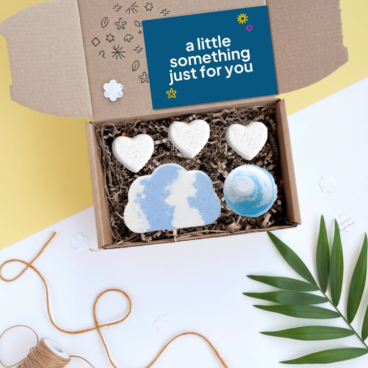 gift box with five bath bombs in the shape of hearts and clouds, on a yellow background with a card that reads ' a little something just for you'