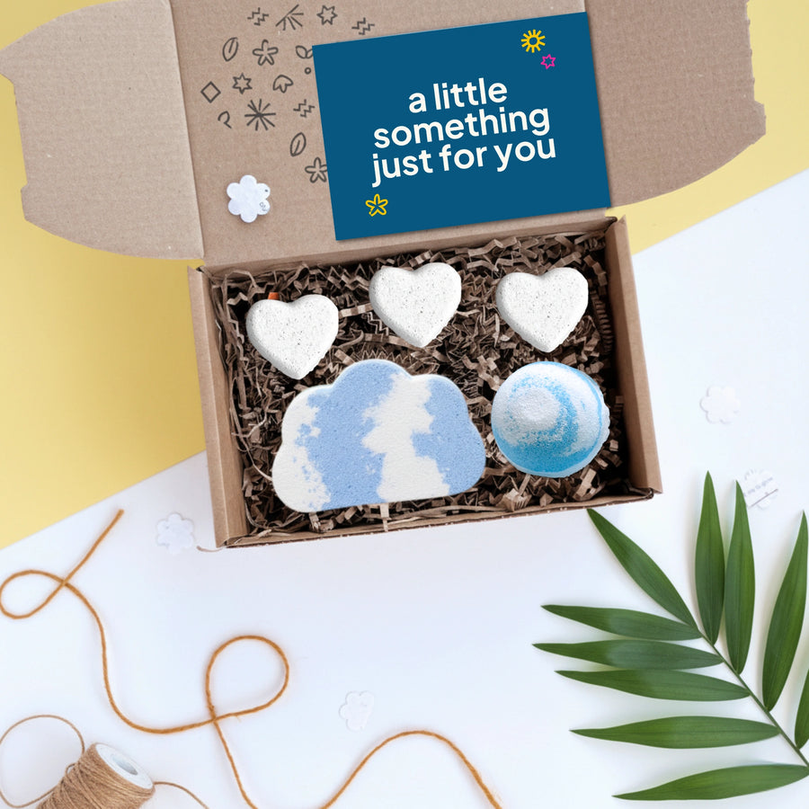 gift box with five bath bombs in the shape of hearts and clouds, on a yellow background with a card that reads ' a little something just for you'