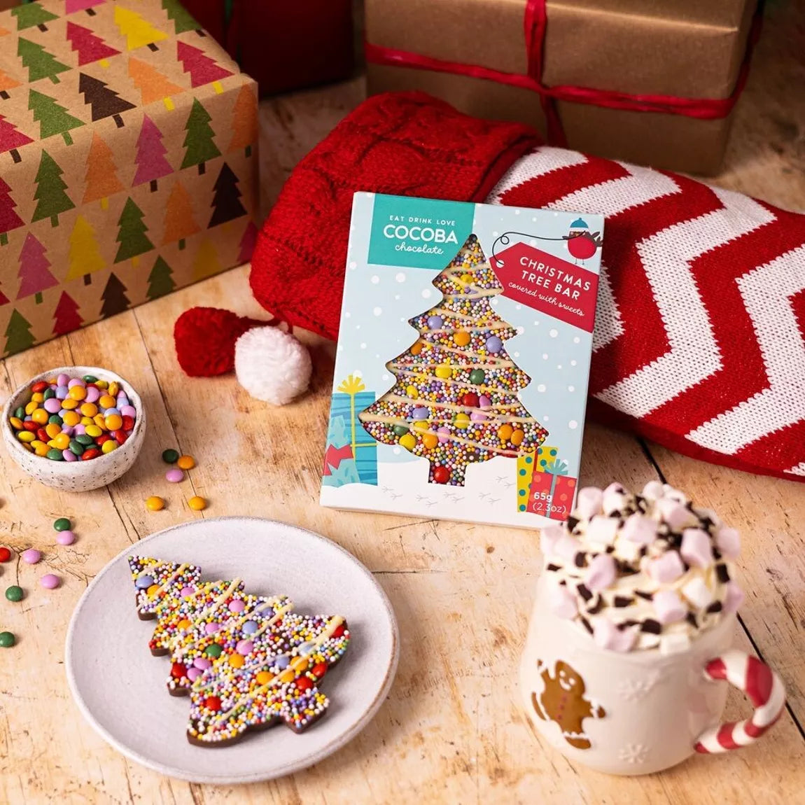 christmas tree loaded chocolate bar by cocoba on a white plate with a hot chocolate mug and bar in packaging. 