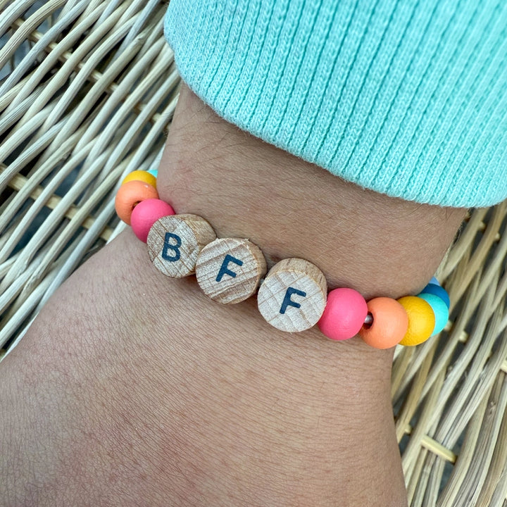 Bracelet with letter beads on a wrist, wearing a light blue beanie jumper.