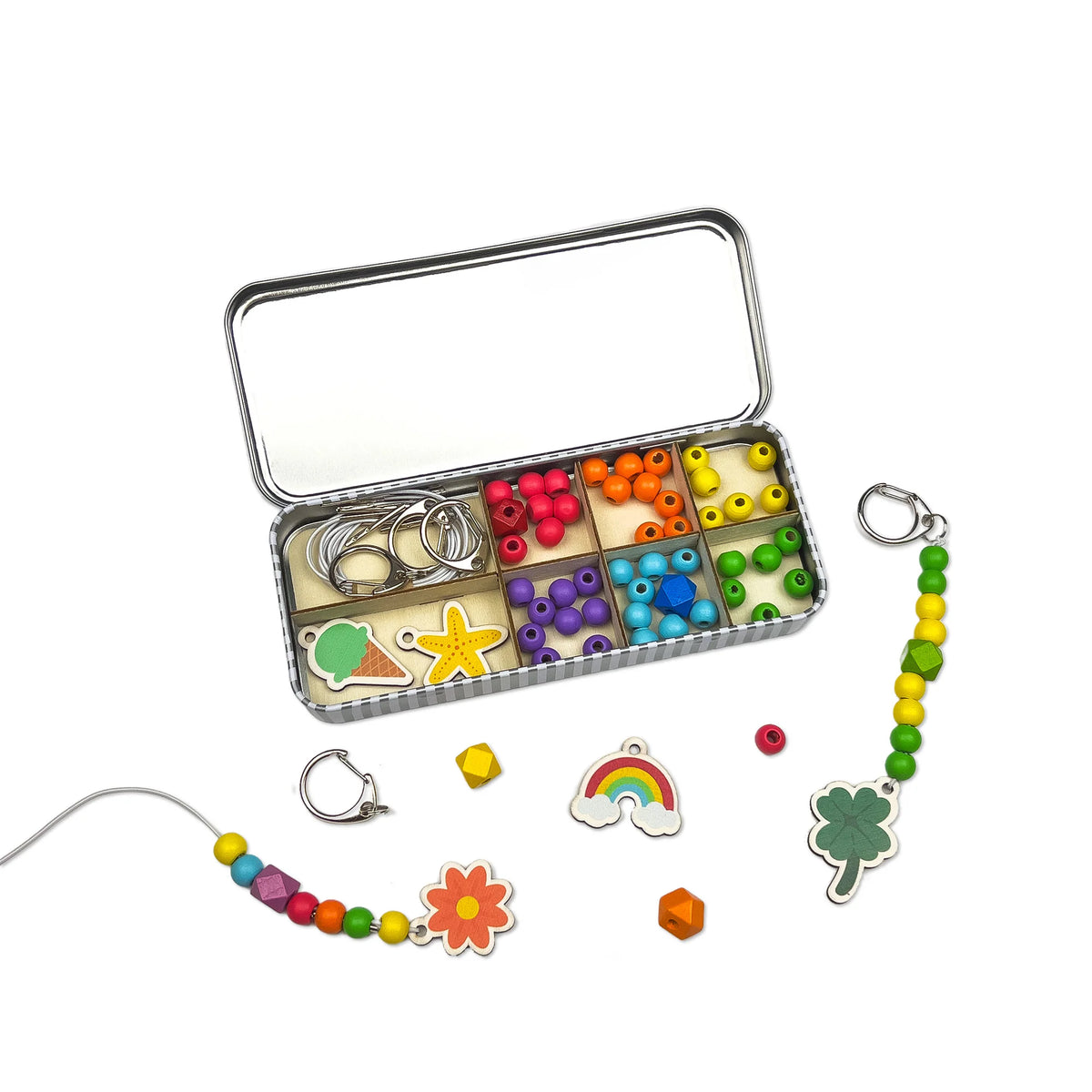 childrens lucky dip keyring making craft kit in a tin. The tin is open displaying an assortment of colourful beads and charms. Two finished keyrings are laid on the white background. 