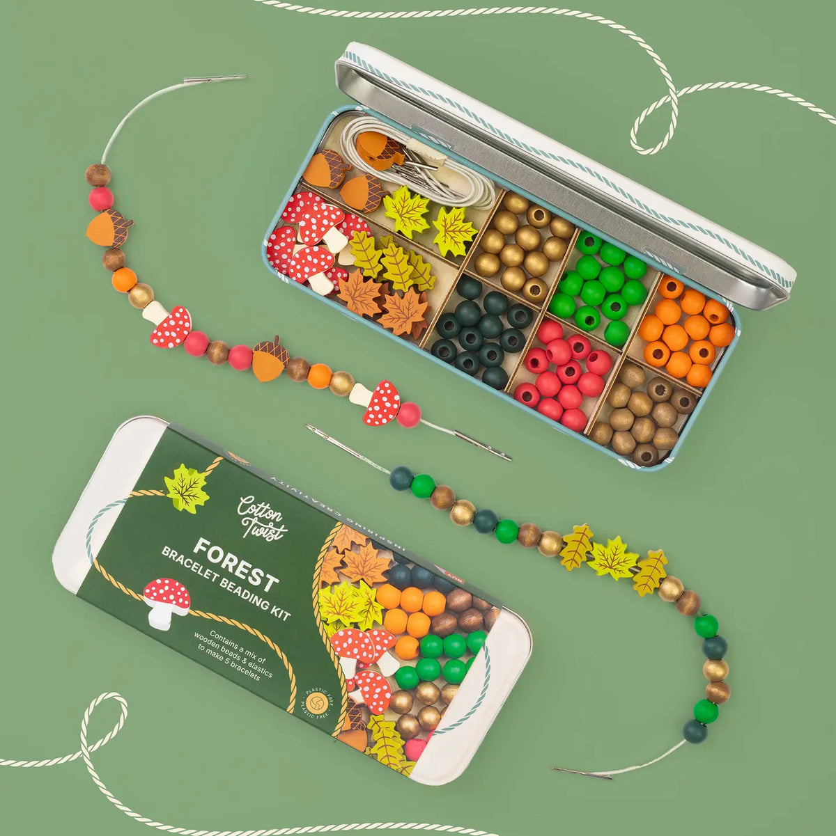 An open metal tin filled with colourful wooden beads and needles, shown alongside a matching branded box labeled 'Cotton Twist Forest Bracelet Beading Kit' on a muted green background.