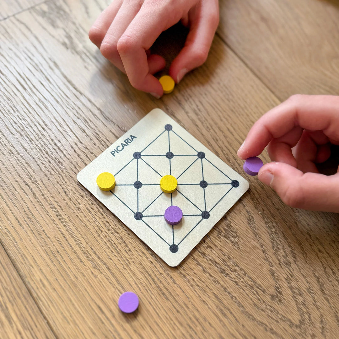Childrens hands playing with Picaria Game board with colourful markers on a wooden surface